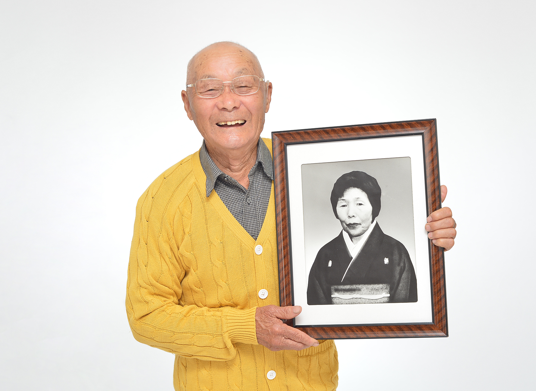 黄色カーディガンを着て、奥様の遺影を持つ80代の男性